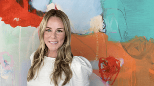 Woman in white standing in front of abstract painting with bold colors