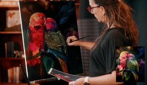 woman painting red and green birds on a canvas 