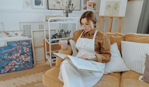 Girl sitting in apron reading book on yellow couch