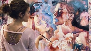 girl standing in front of pastel colored painting holding paintbrush