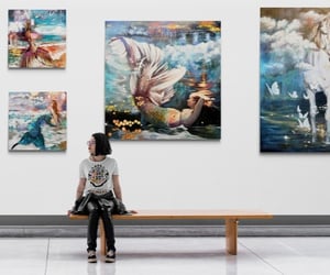 girl sitting in a gallery with mermaid painting on the wall