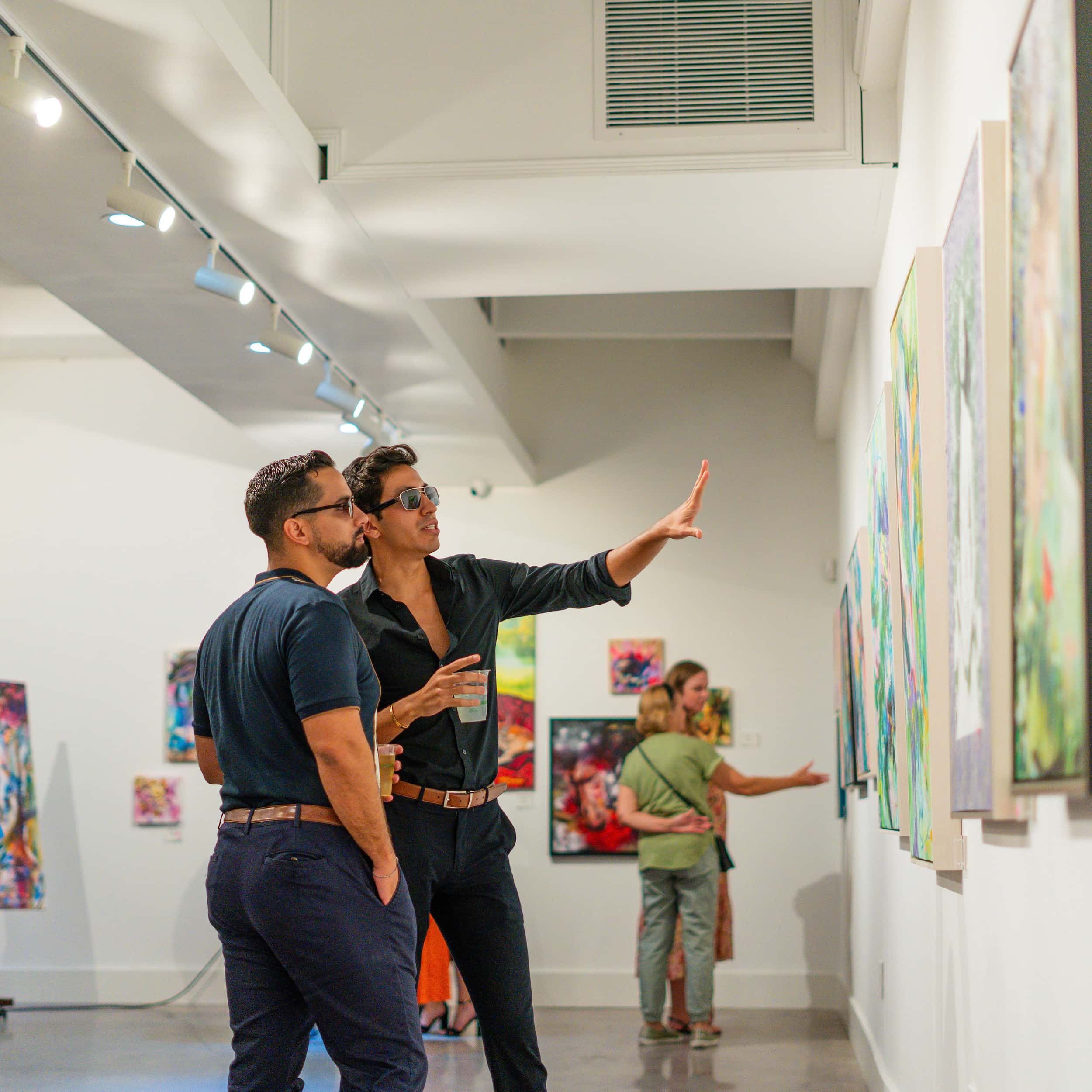 Two people standing in a gallery studying paintings hung on the walls